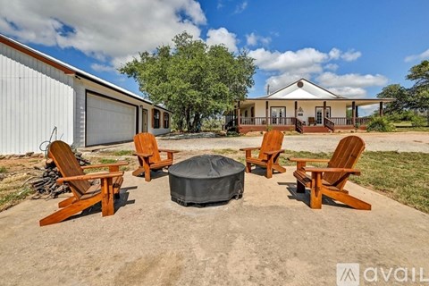 A set of wooden chairs and a round ottoman are arranged on a concrete surface outside a house.