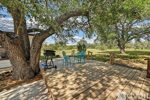 A wooden deck with a grill and chairs under a tree.