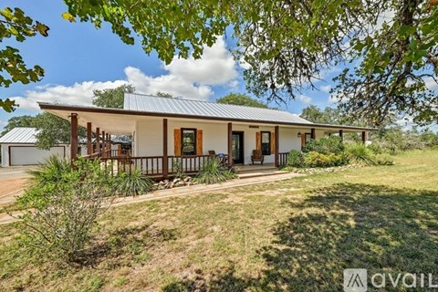 A house with a metal roof and a porch is surrounded by greenery.