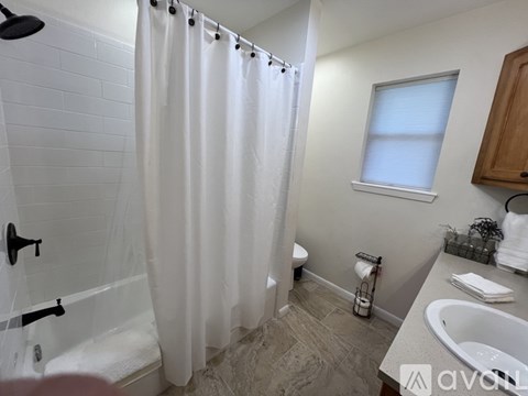 A bathroom with a white shower curtain, a white sink, and a window with blinds.