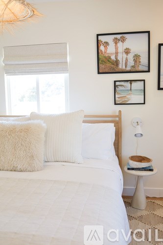A bedroom with a white bed and a picture of palm trees on the wall.