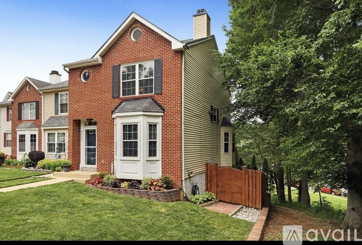 A house with a red brick facade and a white door is surrounded by a well-kept lawn and trees.