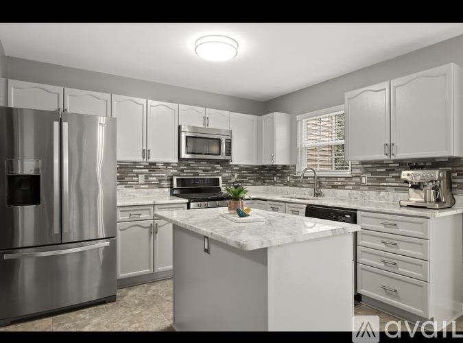 A kitchen with a stainless steel refrigerator and a marble island.