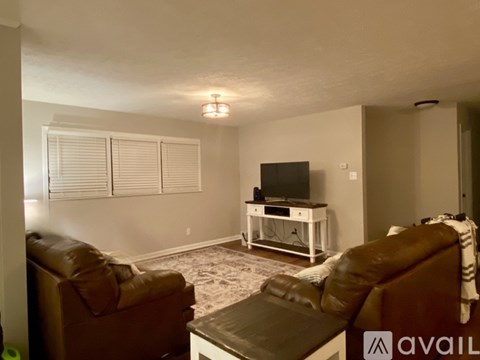 A living room with a brown leather couch, a white entertainment center with a flat screen TV, and a rug on the floor.
