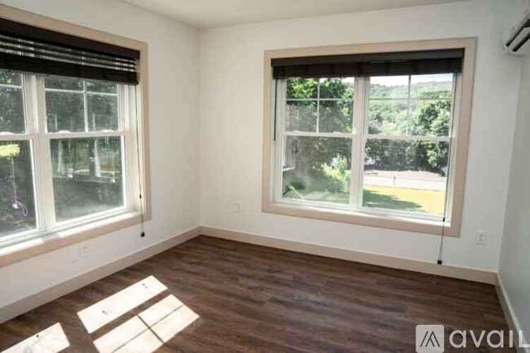 A room with two windows and wooden flooring is available for rent.
