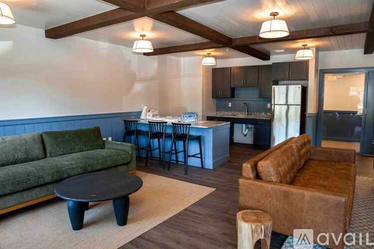 A living room with a green couch, a brown armchair, and a kitchen area in the background.