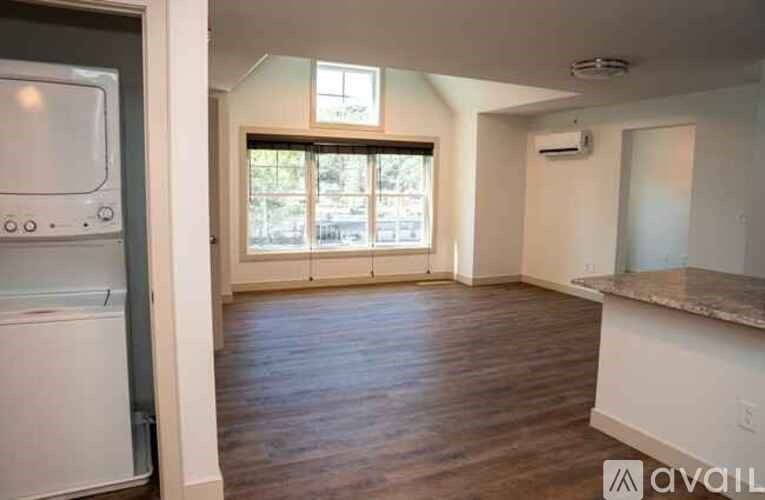 A kitchen with a refrigerator, wooden floors, and a window with blinds.