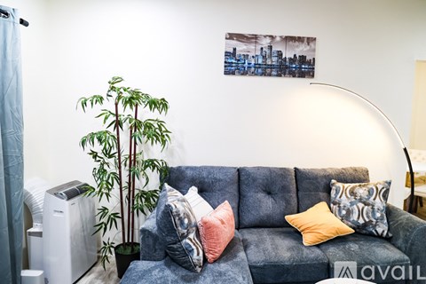 A living room with a grey couch and a potted plant.