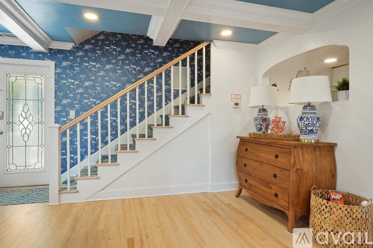 A wooden floor leads up to a staircase with a blue and white wallpapered wall.