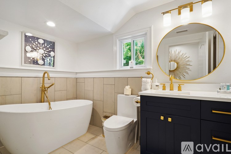 A bathroom with a white tub, black cabinetry, and a gold faucet.