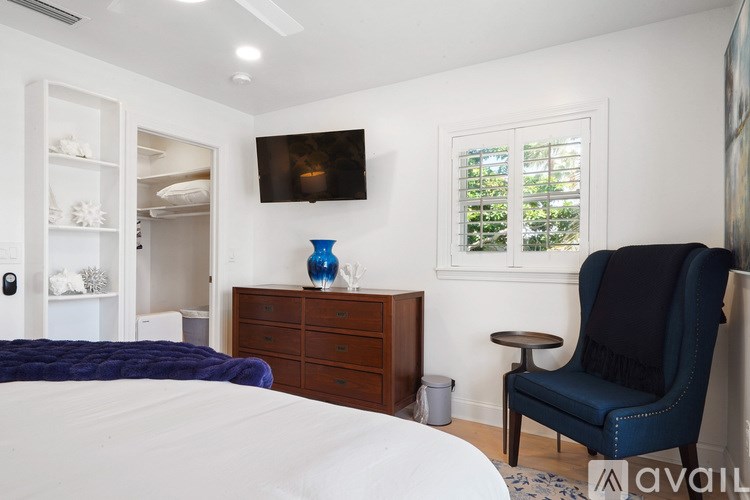 A blue chair sits in a white bedroom with a large bed.