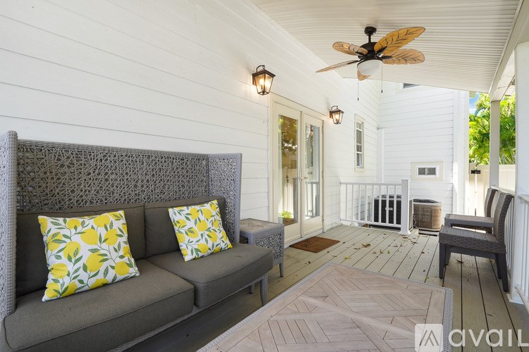 A grey couch with yellow and white pillows is on a porch.