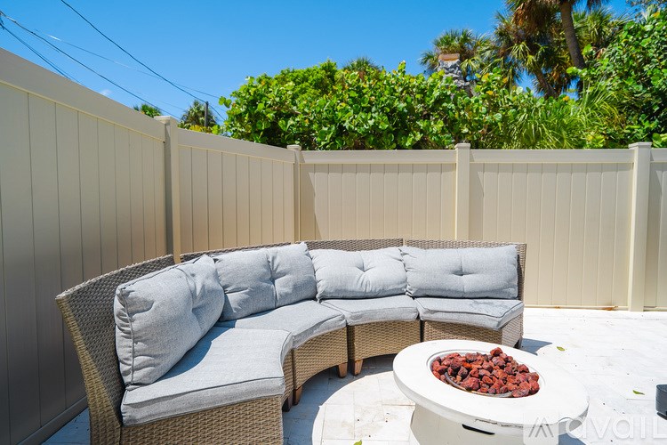 A patio with a grey couch and a white table with red rocks on it.
