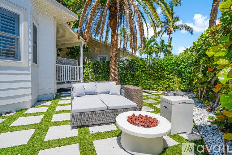 A white outdoor patio with a wicker sofa and a table with a bowl of nuts on it.