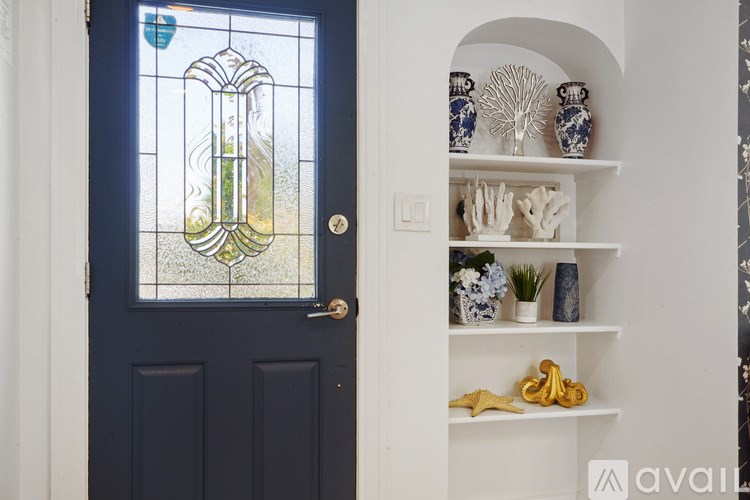 A dark blue door with a stained glass window and a white shelf with decorative items.