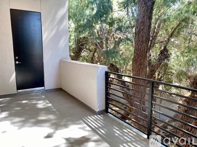 A balcony with a black door and a metal railing with trees in the background.