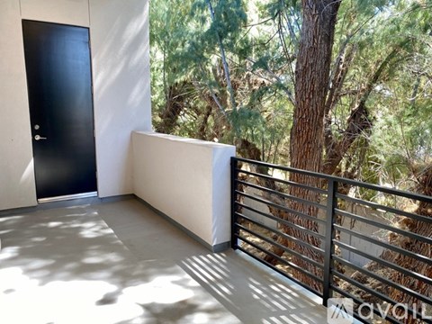 A balcony with a black door and a metal railing with trees in the background.