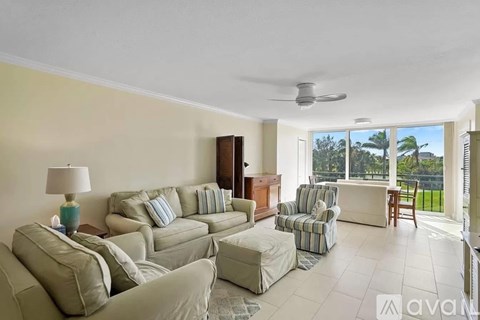 A living room with a white ceiling fan and a large window with a view of trees.