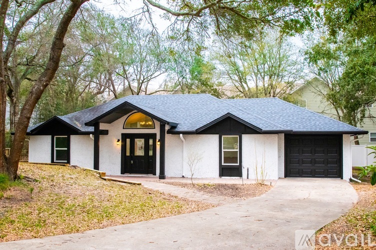 A house with a black roof and white walls is surrounded by trees.
