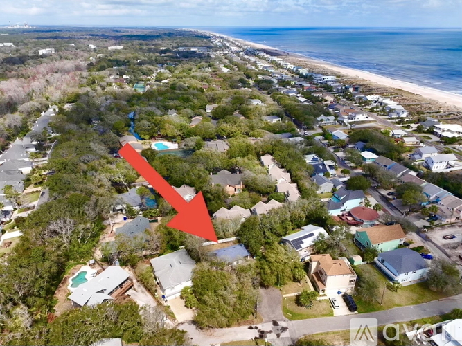 An aerial view of a beachfront neighborhood with a red arrow pointing to a specific house.