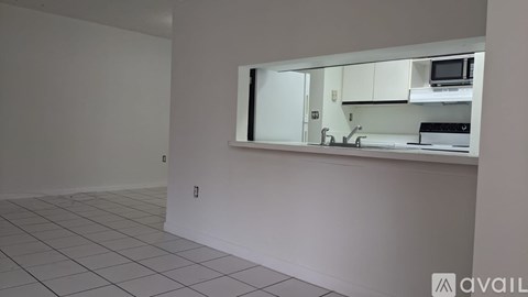 A kitchen with white cabinets and appliances is visible through a window in the wall.