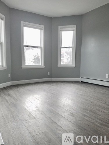 A room with grey walls and wooden flooring with two windows.