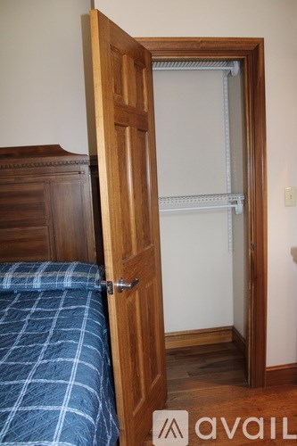 A bedroom with a bed and a wooden wardrobe with an open door.