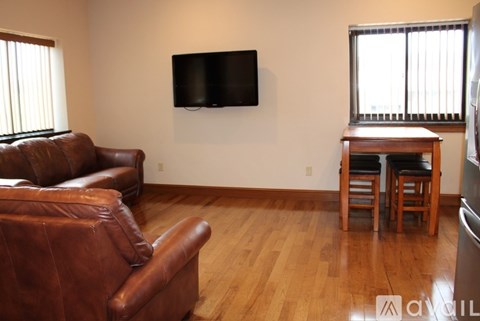 A living room with a brown leather couch and a television mounted on the wall.