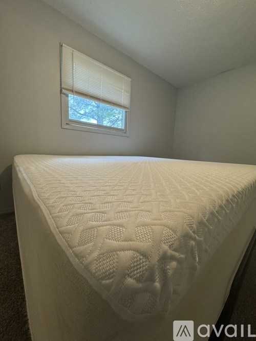 A white bed with a quilted mattress pad in a room with a window.