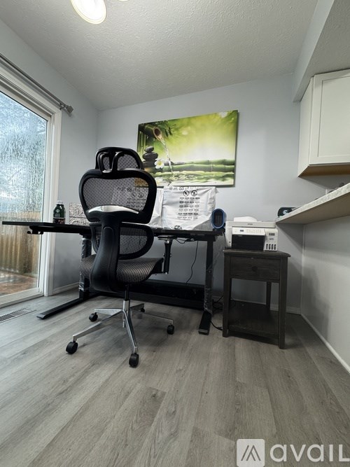 A black office chair is in front of a desk with a laptop and a printer.