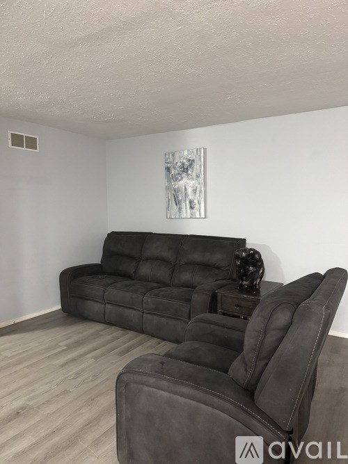 A black leather sofa in a room with a wooden floor and a painting on the wall.