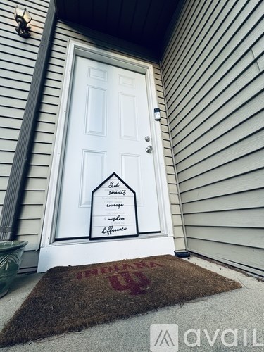 A white door with a sign on it and a doormat with the letters "INDIANA" on it.