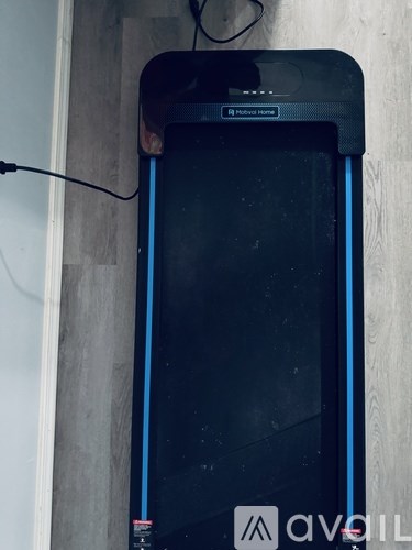 A black treadmill with a blue handle is placed against a wooden wall.