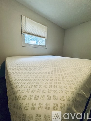 A bed with a white mattress and a window with blinds.
