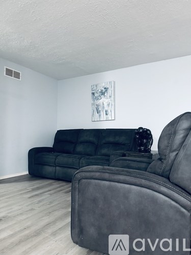 A black leather couch and chair in a room with a painting on the wall.