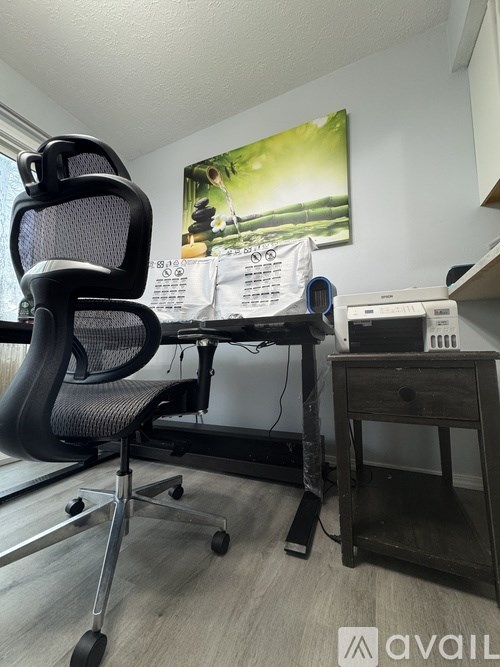 A black office chair is in front of a desk with a printer and a calendar.