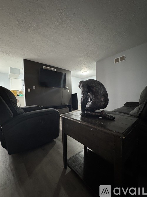 A person is sitting on a black leather chair in a room with a television and a wooden table.