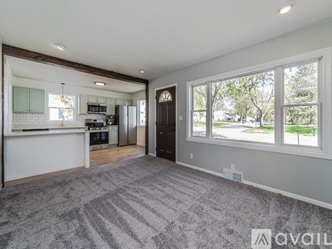 A spacious living room with a kitchen in the background and a grey carpet on the floor.