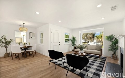 A living room with a black and white checkered rug, a black chair, a wooden dining table with chairs, and a fireplace.