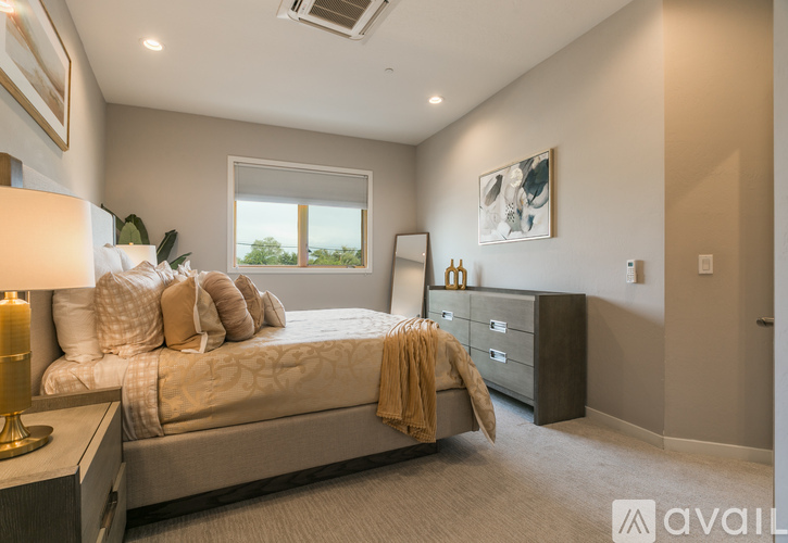 A well-lit bedroom with a large bed, a nightstand with a lamp, and a window with a view of the outdoors.