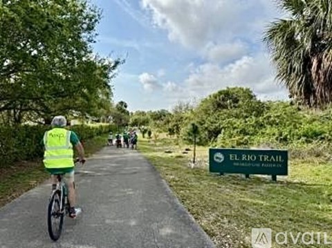 A person on a bicycle is riding on a paved trail next to a sign that says "El Rio Trail".