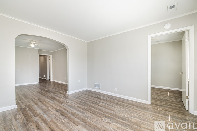 A room with wood flooring and white walls, with a doorway leading to another room.