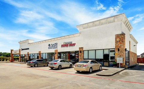 A car dealership with a white building and two cars parked in front.
