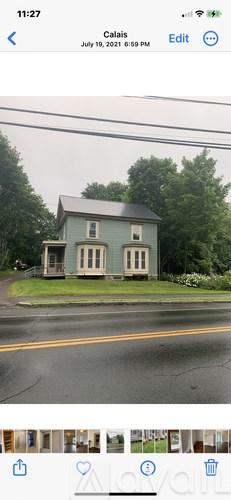 A blue house with white trim is situated on a street with a yellow line.