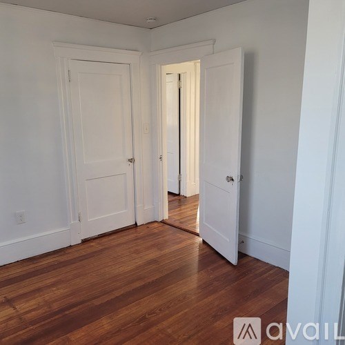 A room with white walls and wooden floors, with a door on the right.