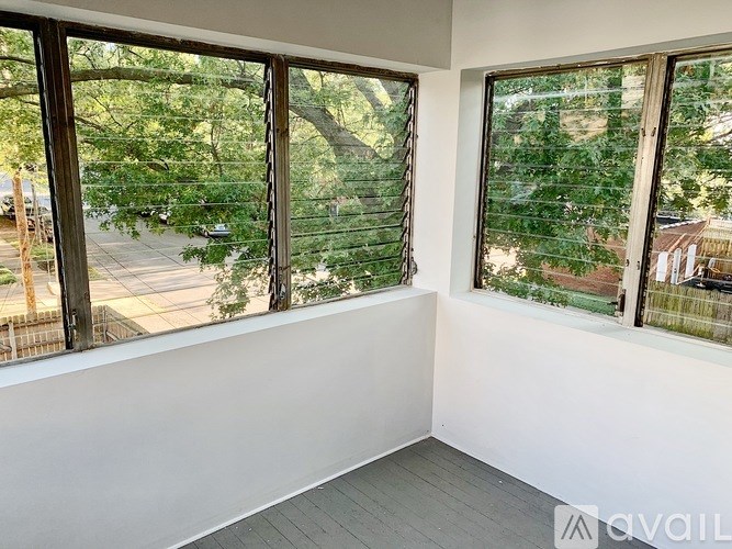 A room with two windows overlooking a tree-filled street.