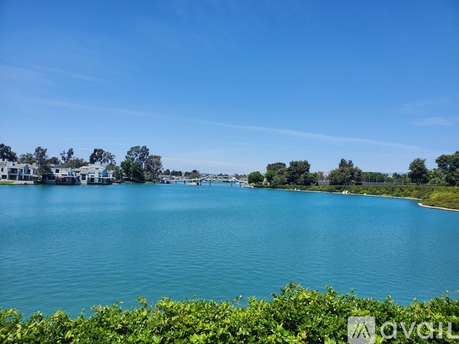 A serene lake surrounded by lush greenery and buildings in the distance under a clear blue sky.