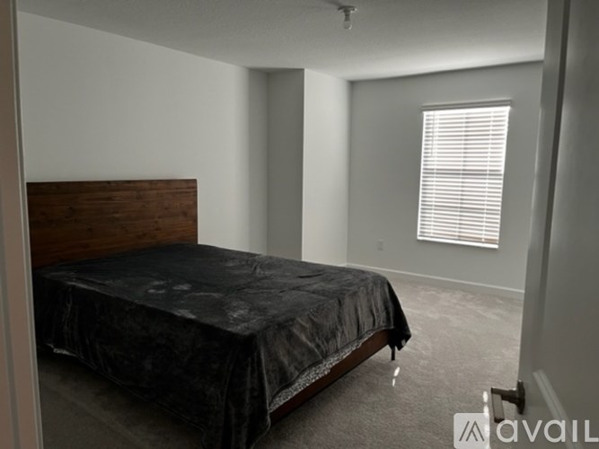 A bedroom with a bed covered in a black sheet and a window with blinds.