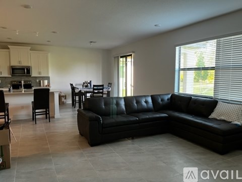 A black leather sofa sits in a spacious living room with a kitchen in the background.