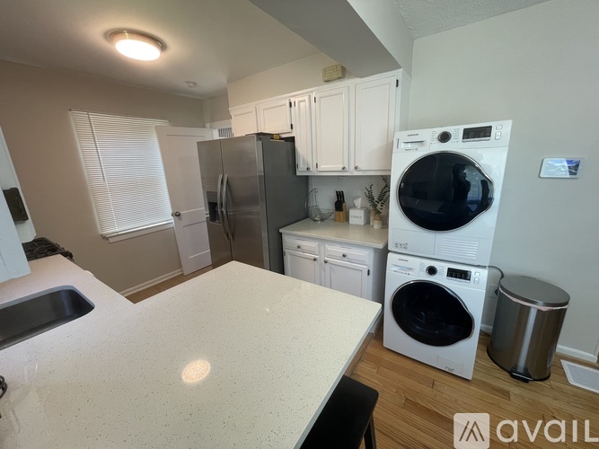 A kitchen with a white counter top and a washer and dryer stacked on top of each other.